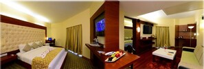 A hotel room with a bed, a desk with a fruit plate, a television, and a small seating area.