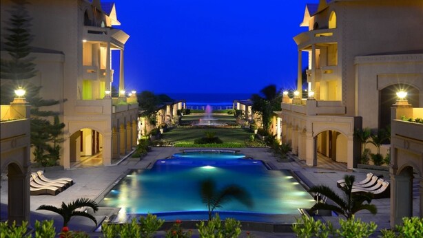 A resort with a swimming pool, multiple buildings, and a view of the sea at dusk. - The Chariot Resort & Spa (Puri)