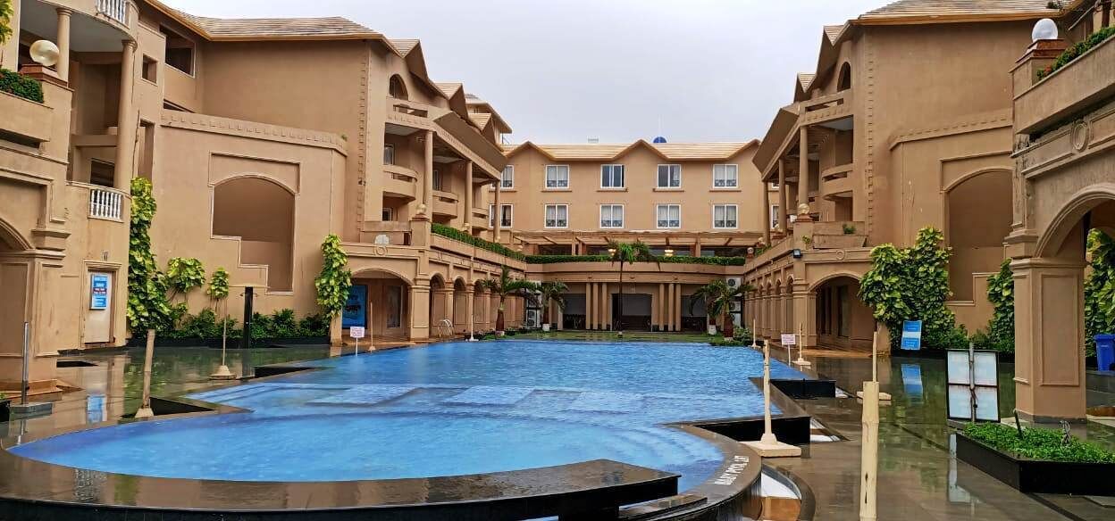 A hotel courtyard with a central pool, multiple balconies, and lush greenery.