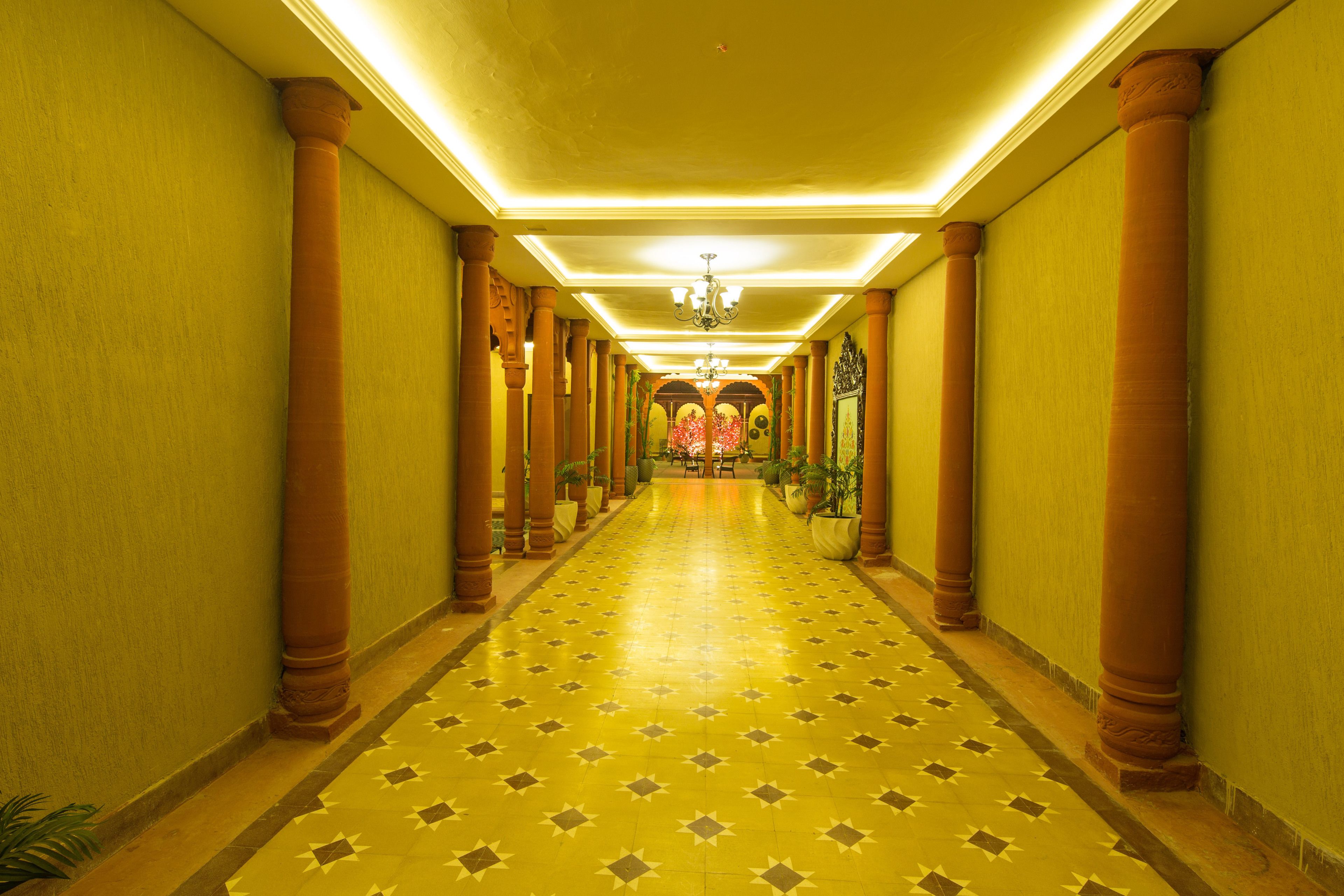 A long, narrow hallway with a patterned floor, columns, and a chandelier.