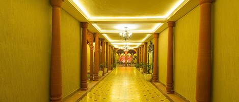 A long, narrow hallway with a patterned floor, columns, and a chandelier.