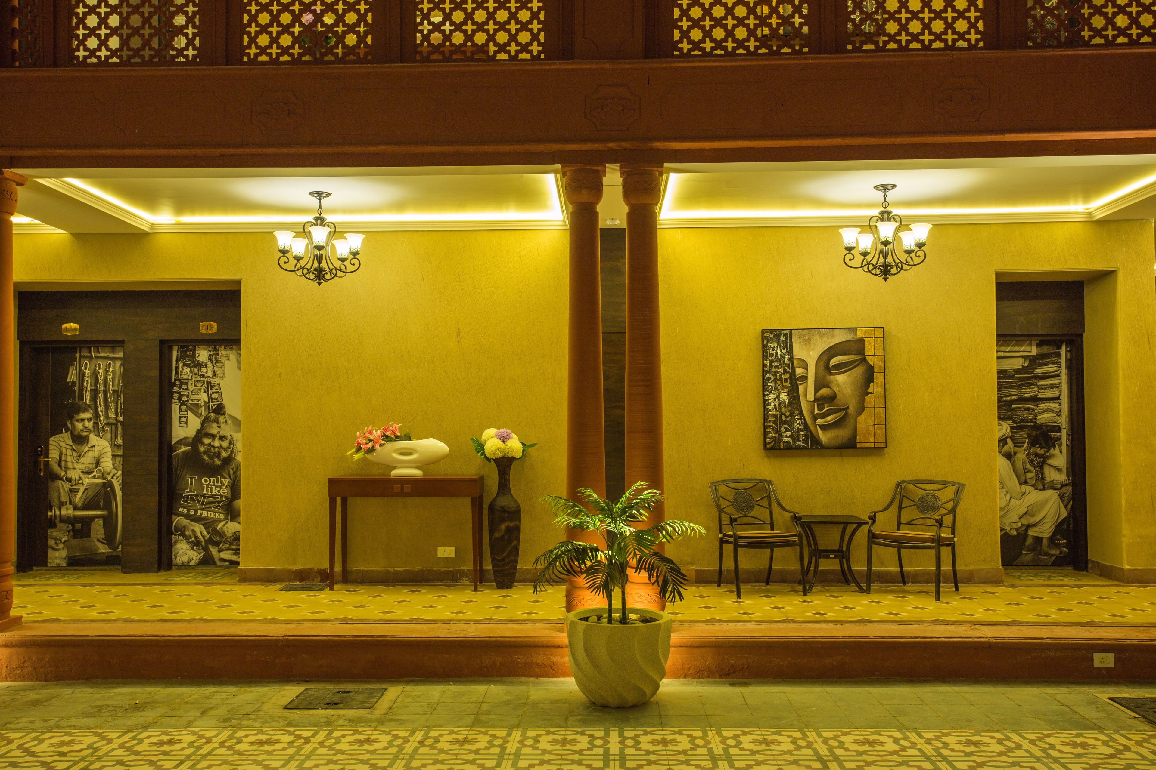 Un hall d’entrée avec une grande plante en pot, deux fauteuils, une table avec un vase et un tableau accroché au mur.