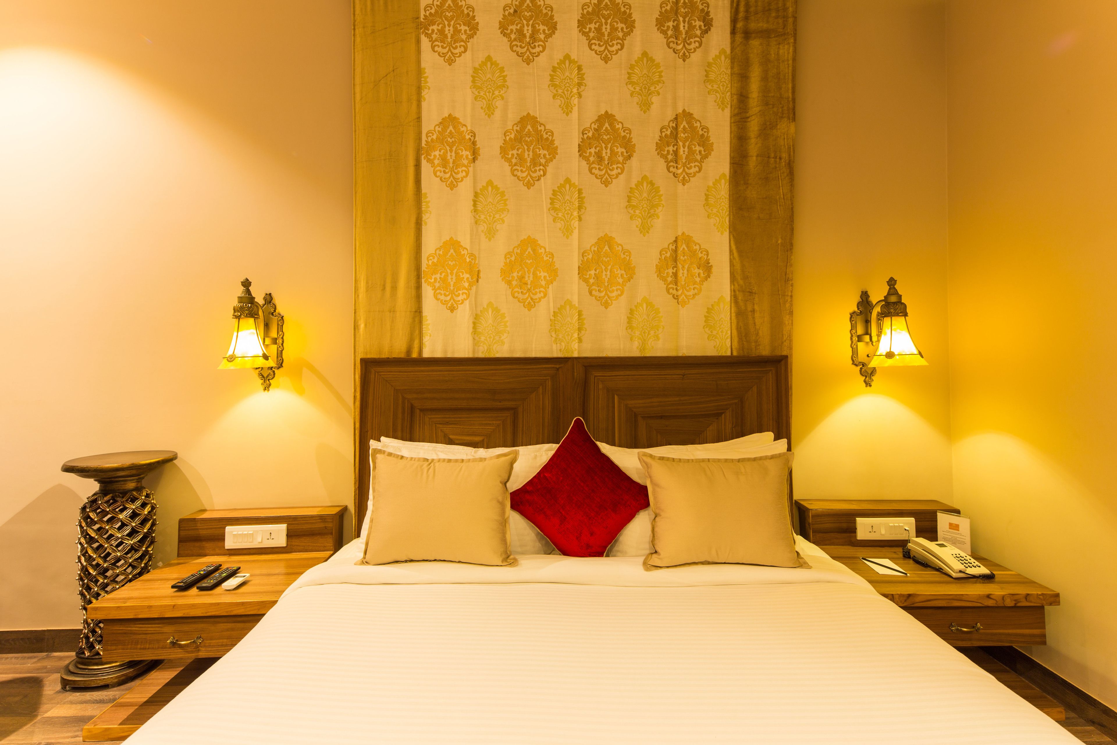 Une chambre d’hôtel avec un grand lit, deux tables de chevet, une lampe, un téléphone et un coussin décoratif rouge.