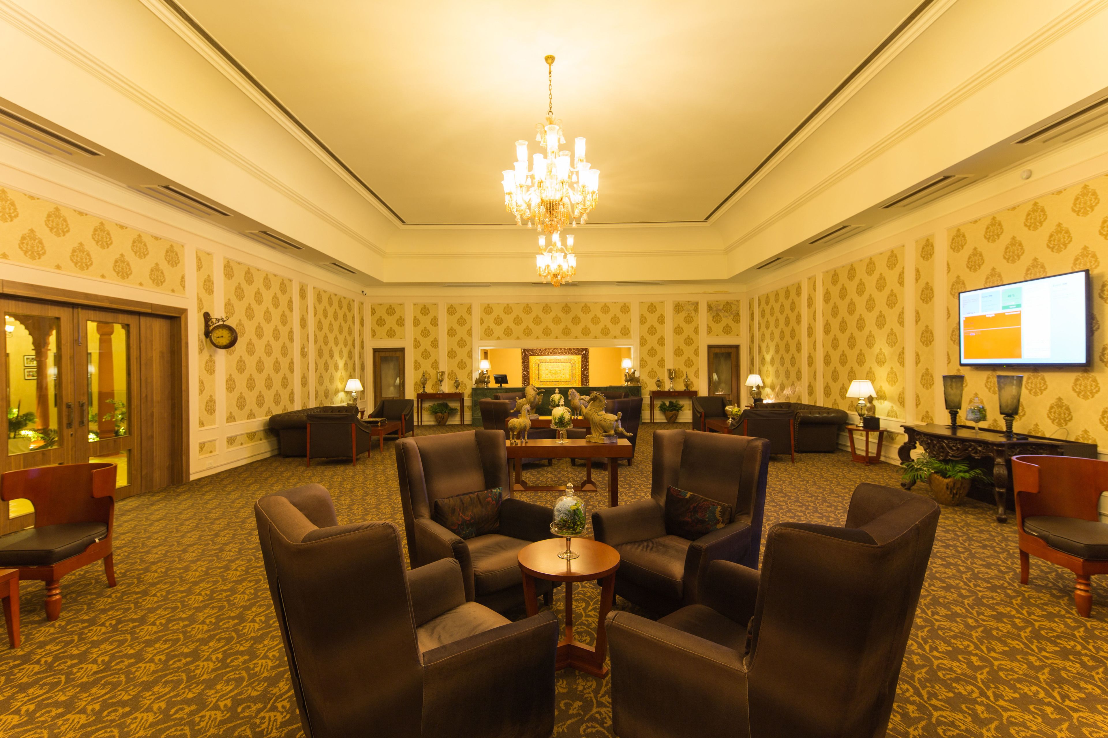 A spacious lobby with a chandelier, comfortable seating, a television, and a reception desk.