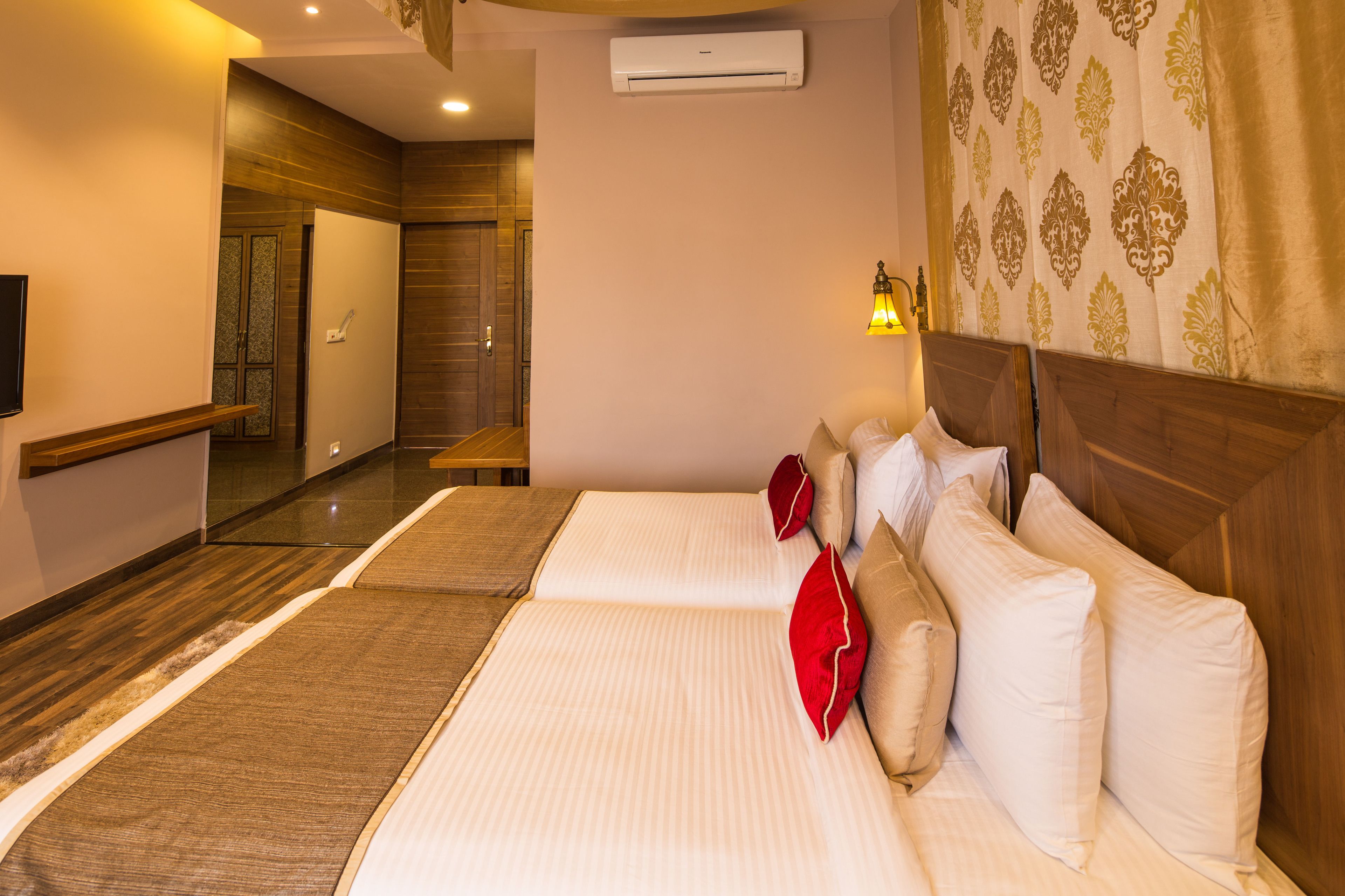 A hotel room with two beds, a wooden headboard, a wall-mounted air conditioner, and a patterned curtain.