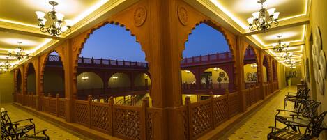 A corridor with ornate wooden arches, chandeliers, and patterned flooring.
