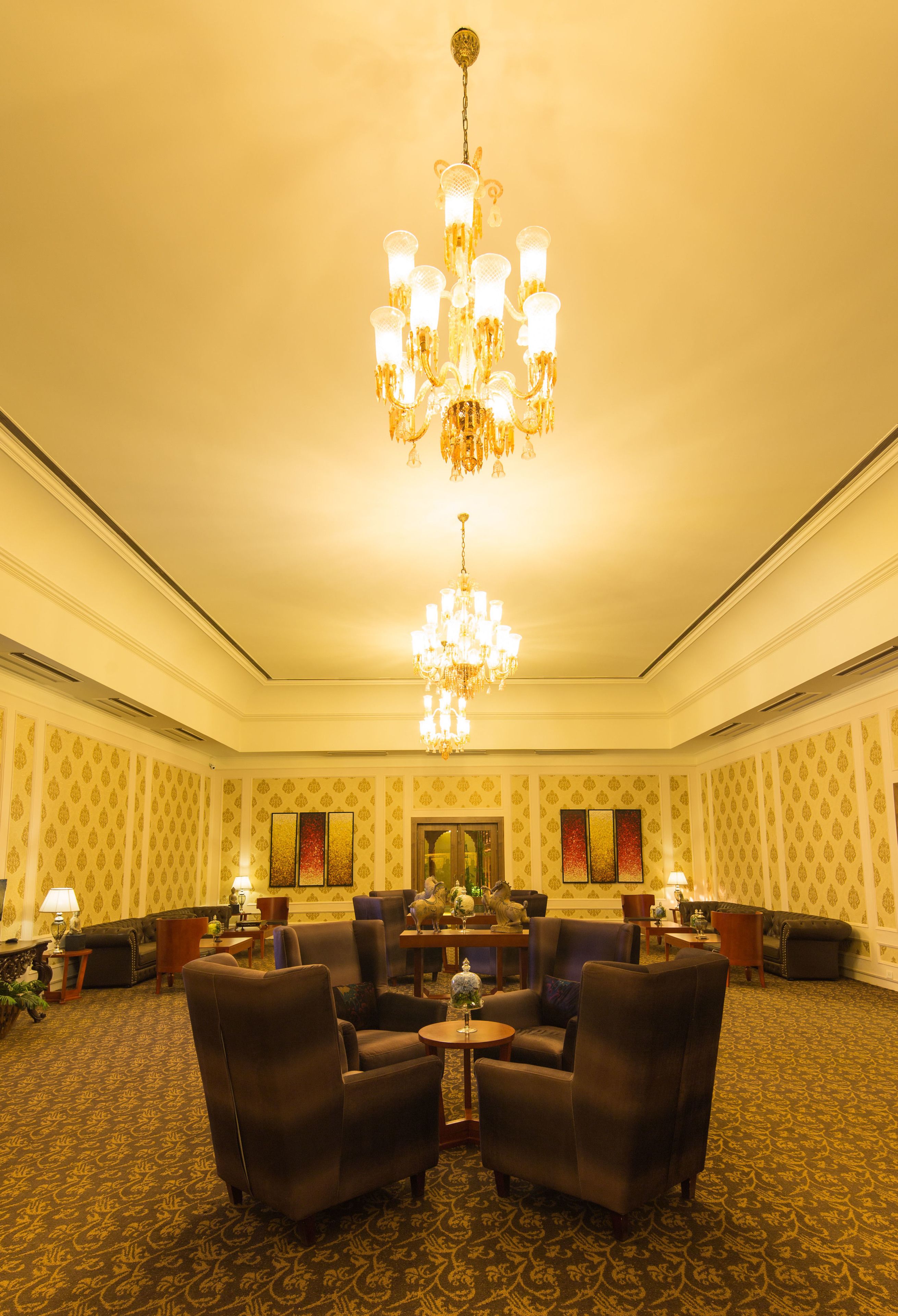 A spacious room with a large chandelier, multiple seating areas, and a patterned carpet.