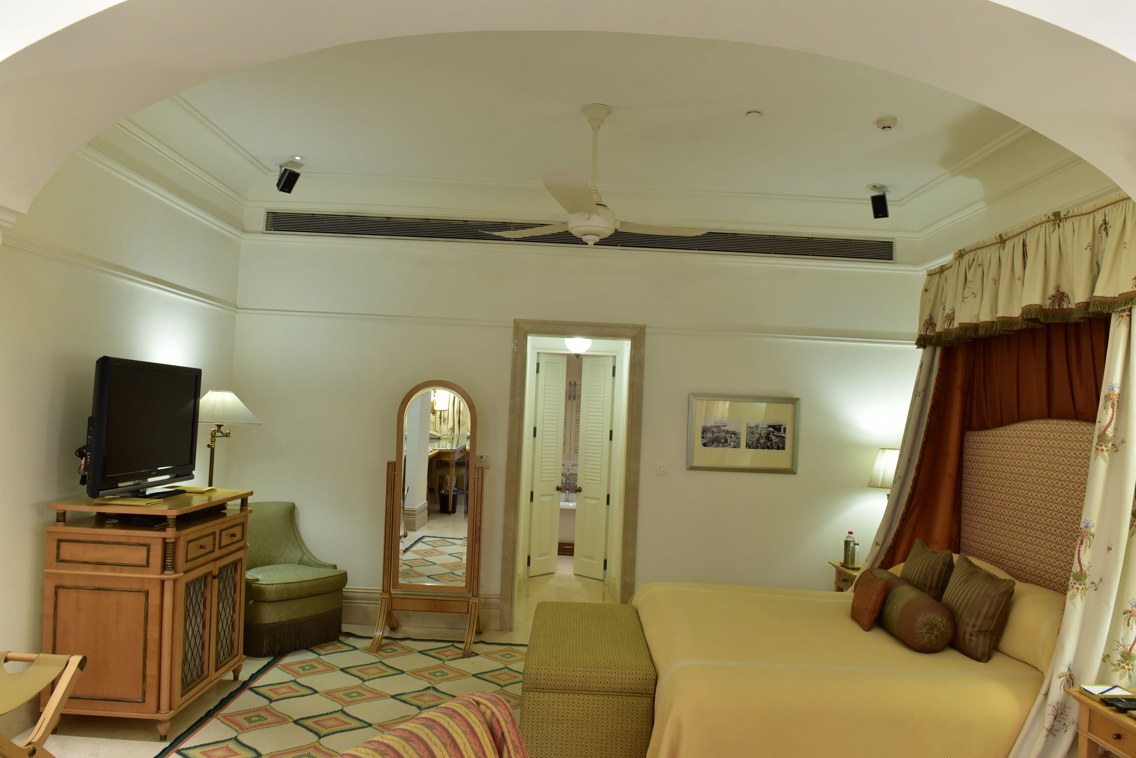 Une chambre d’hôtel comprenant un lit, une télévision, une armoire, un miroir et une salle de bain visible à travers une arche.