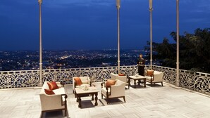A covered outdoor seating area with ornate metalwork and a view of a cityscape at dusk. - Taj Falaknuma Palace (Hyderabad)