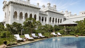 A large white building with multiple domes and arches, a swimming pool with sun loungers, and lush greenery. - Taj Falaknuma Palace (Hyderabad)