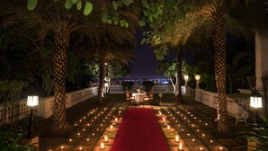 An outdoor dining area with a red carpet, candle-lit tables, and palm trees. - Taj Falaknuma Palace (Hyderabad)
