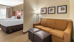 A hotel room with a bed, a sofa, a lamp, and framed pictures on the wall. - Comfort Suites Medical Center near Six Flags (San Antonio)