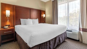A hotel room with a large bed, bedside lamps, a nightstand, and a window with curtains. - Comfort Suites Medical Center near Six Flags (San Antonio)