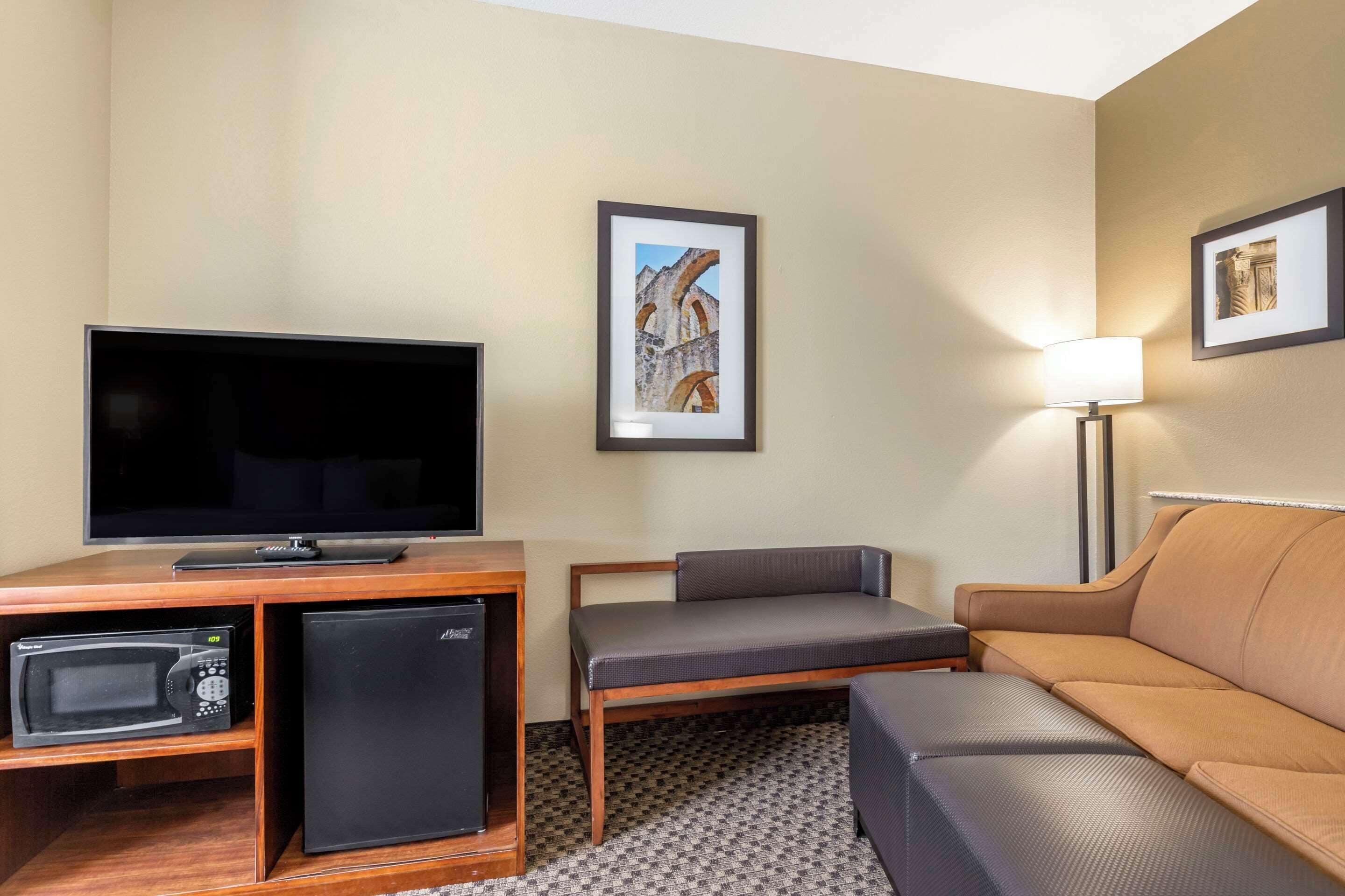 Een hotelkamer met een flatscreen televisie, een minibar, een magnetron, een bank en twee ingelijste foto's aan de muur.