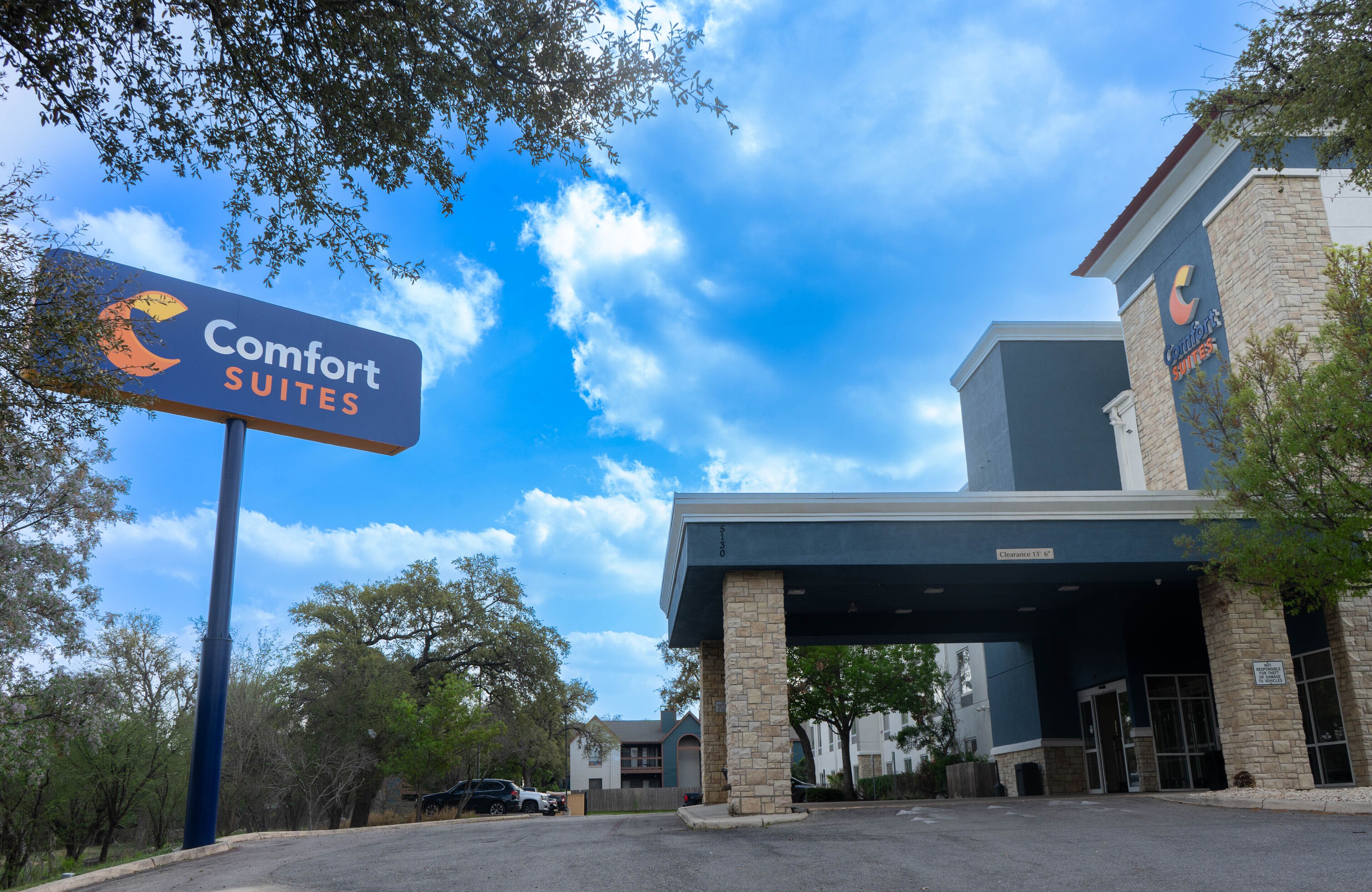 Entrada de um hotel Comfort Suites, com céu azul e árvores ao fundo.