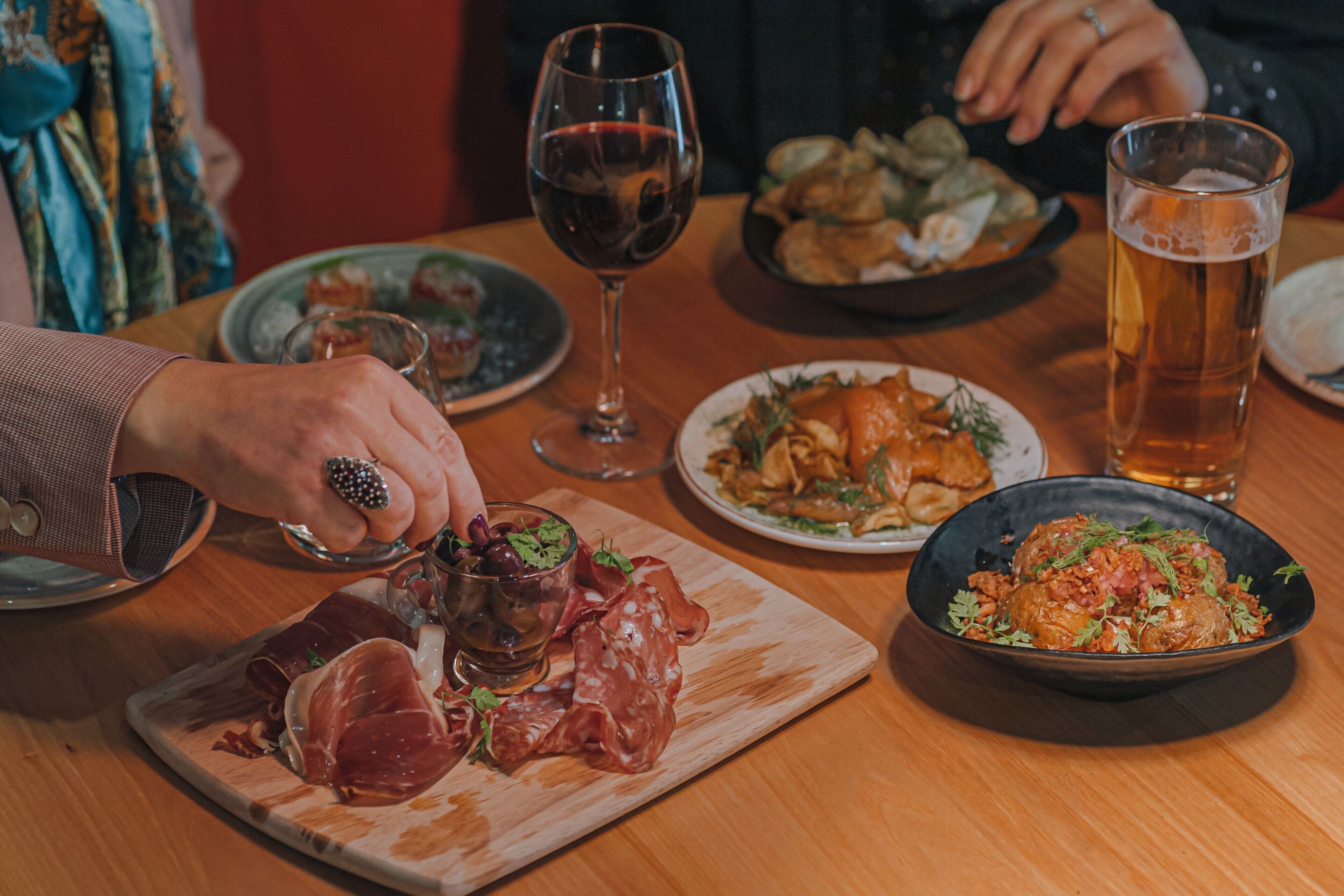 A dining table with various dishes, including a plate of prosciutto, a bowl of salad, and a glass of beer.