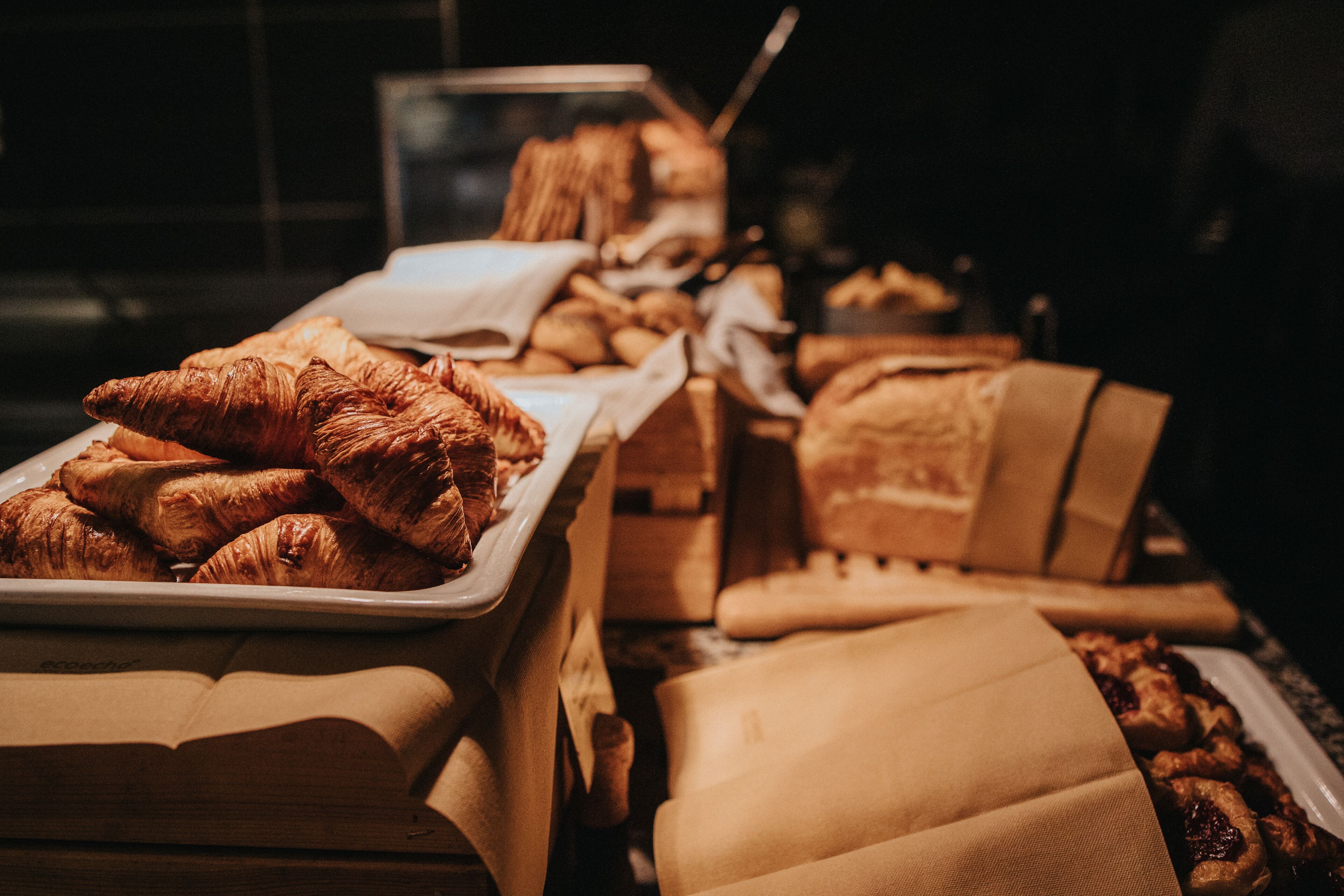 Una exhibición de productos horneados, incluyendo croissants y otras pastelerías, dispuestas en bandejas y cajas.