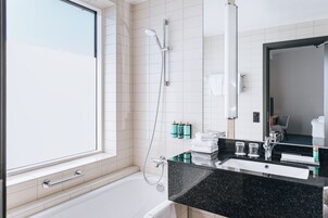 Un baño moderno con bañera, ducha, un espejo grande y tocador con encimera negra.