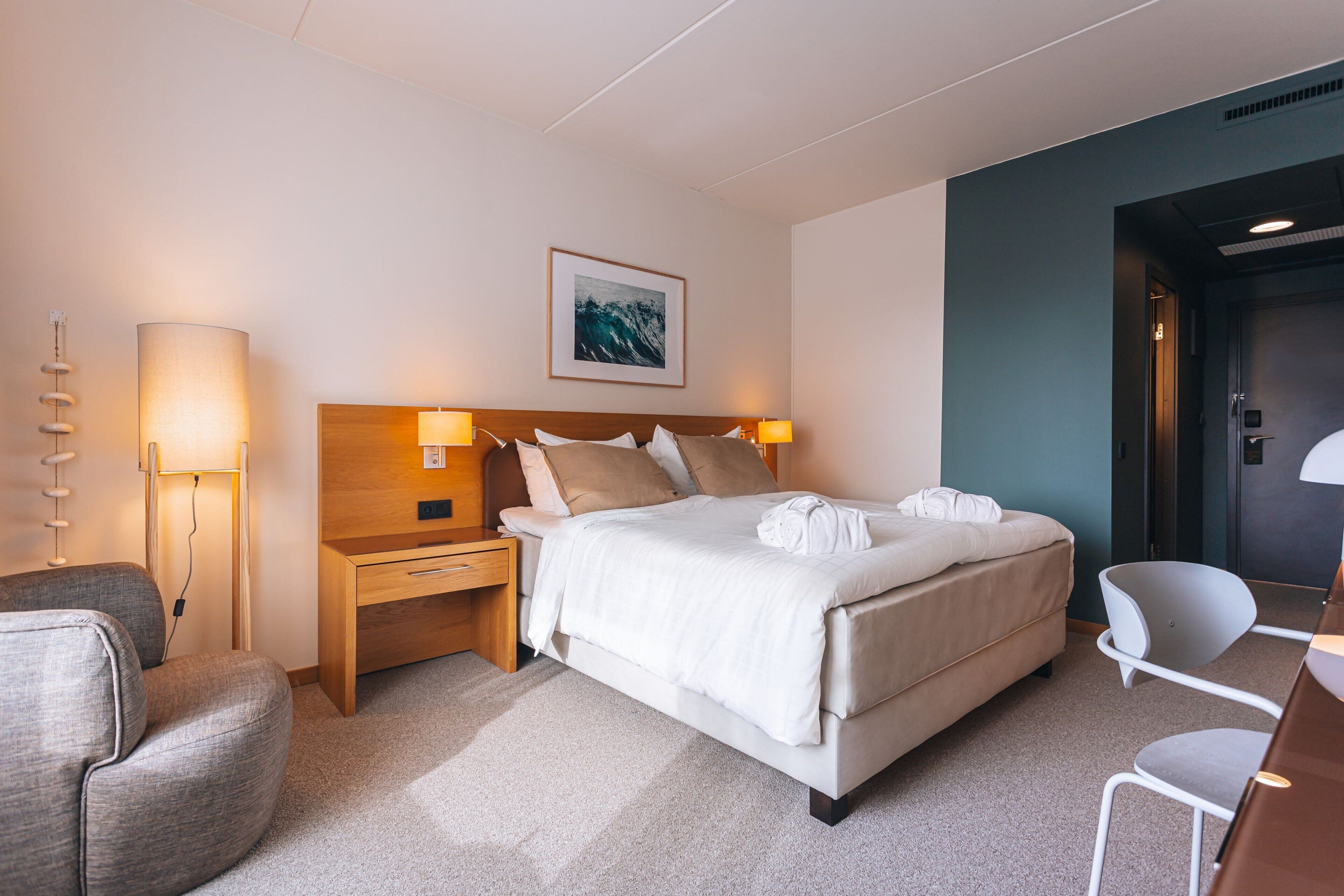 A modern hotel room with a large bed, bedside tables, a desk, and a chair.