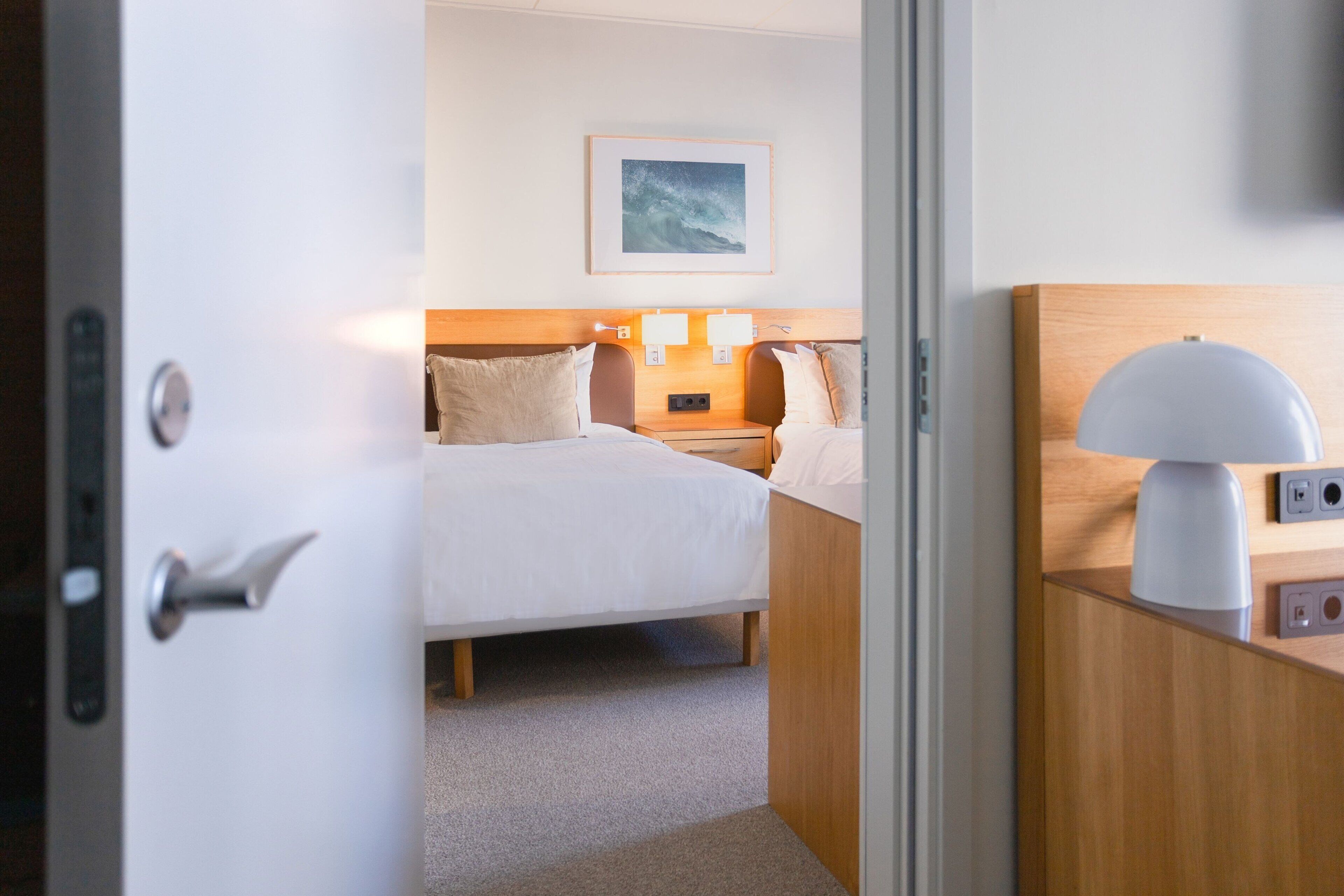Una habitación de hotel con una cama, mesitas de noche, una lámpara y un cuadro en la pared.