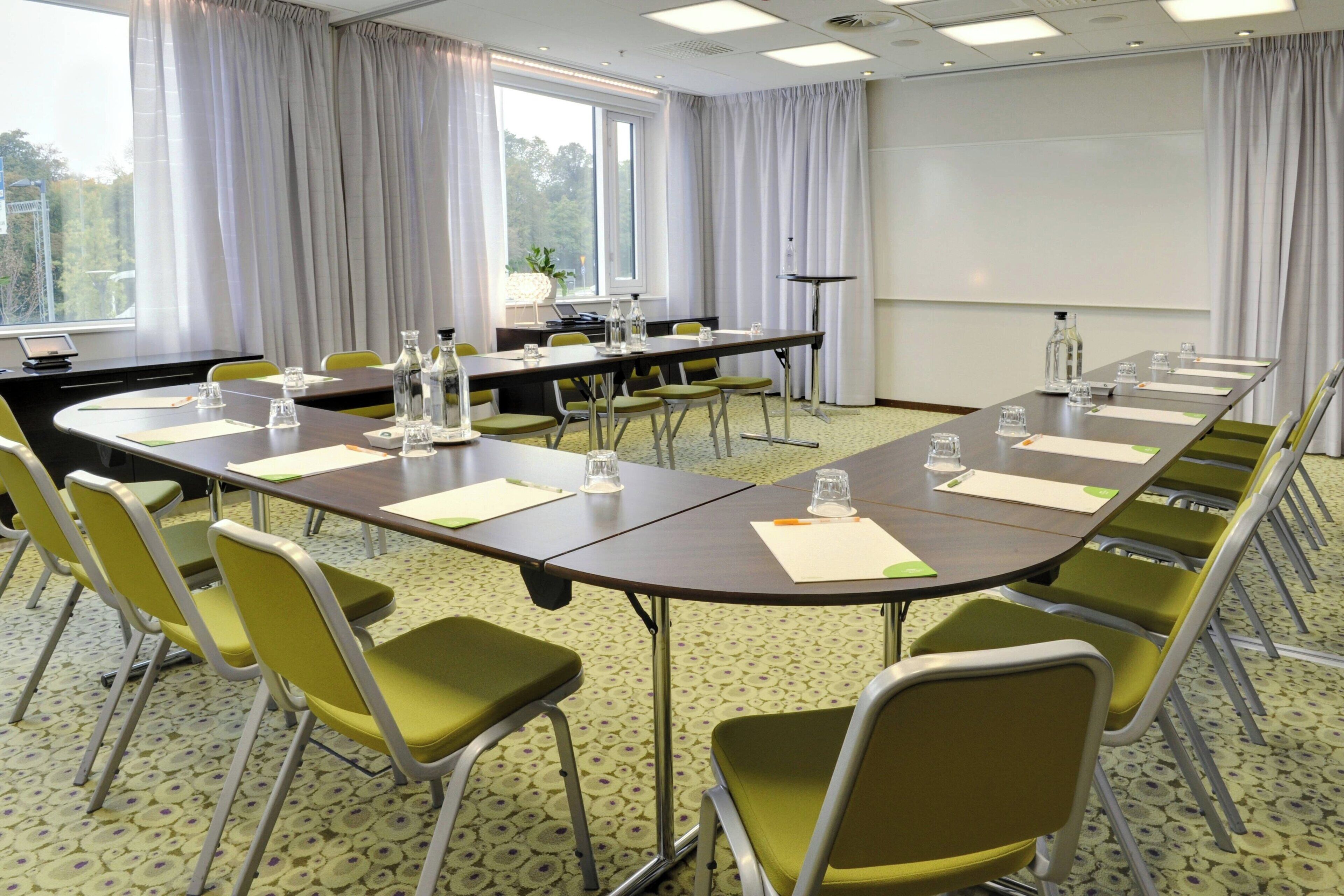 A conference room with a long table, green chairs, and a projector screen.