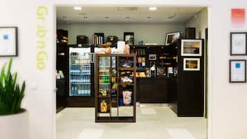 Interior de una tienda con un letrero que dice 'Grab n Go', estantes llenos de bocadillos, un refrigerador con bebidas y fotografías enmarcadas en la pared.