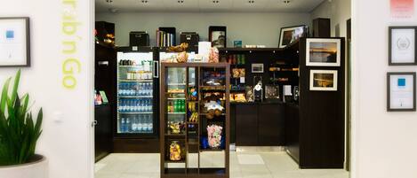 Interior de una tienda con un letrero que dice 'Grab n Go', estantes llenos de bocadillos, un refrigerador con bebidas y fotografías enmarcadas en la pared.
