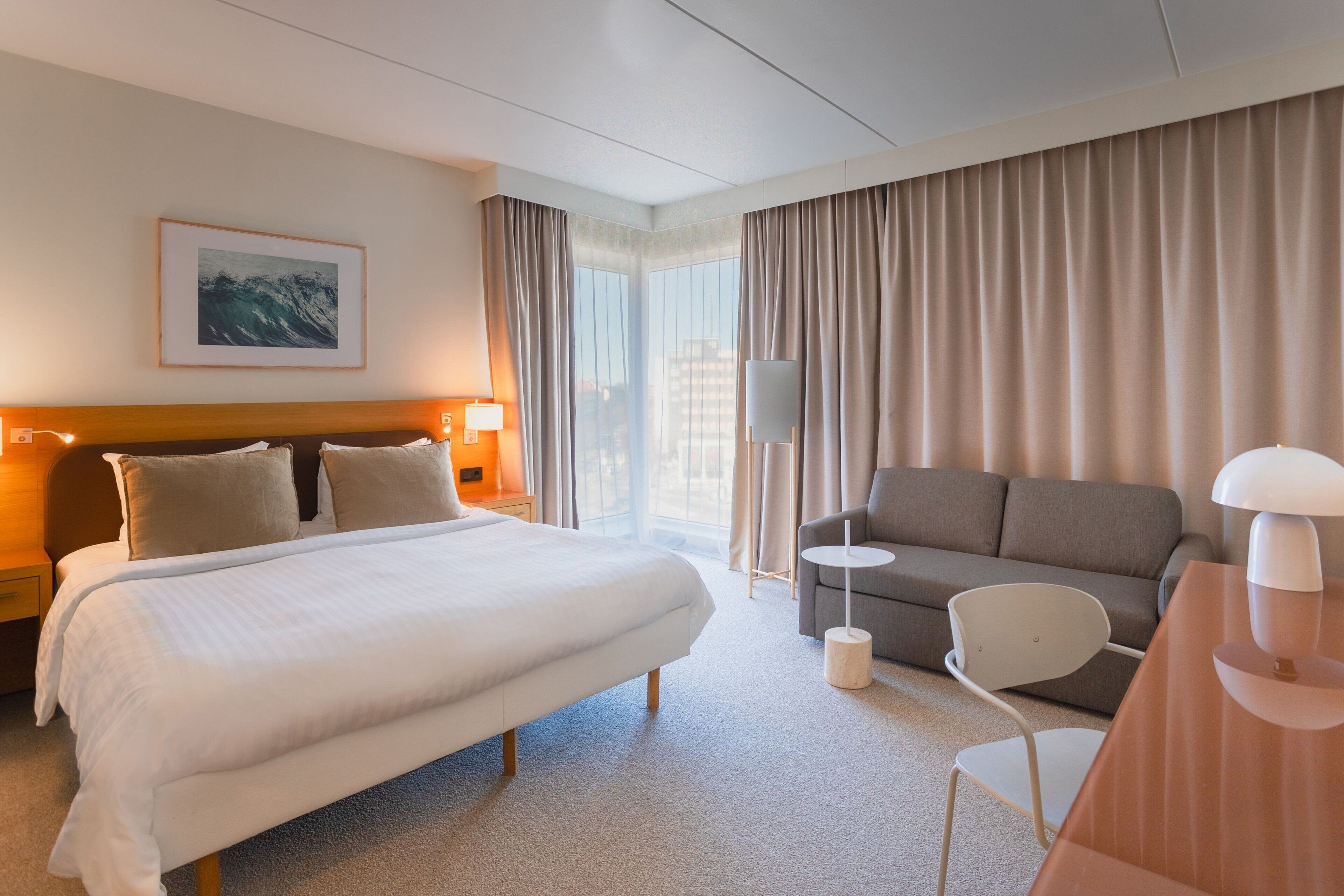 Ett hotellrum med en stor säng, en soffa, ett litet bord, en lampa och en tavla på väggen.