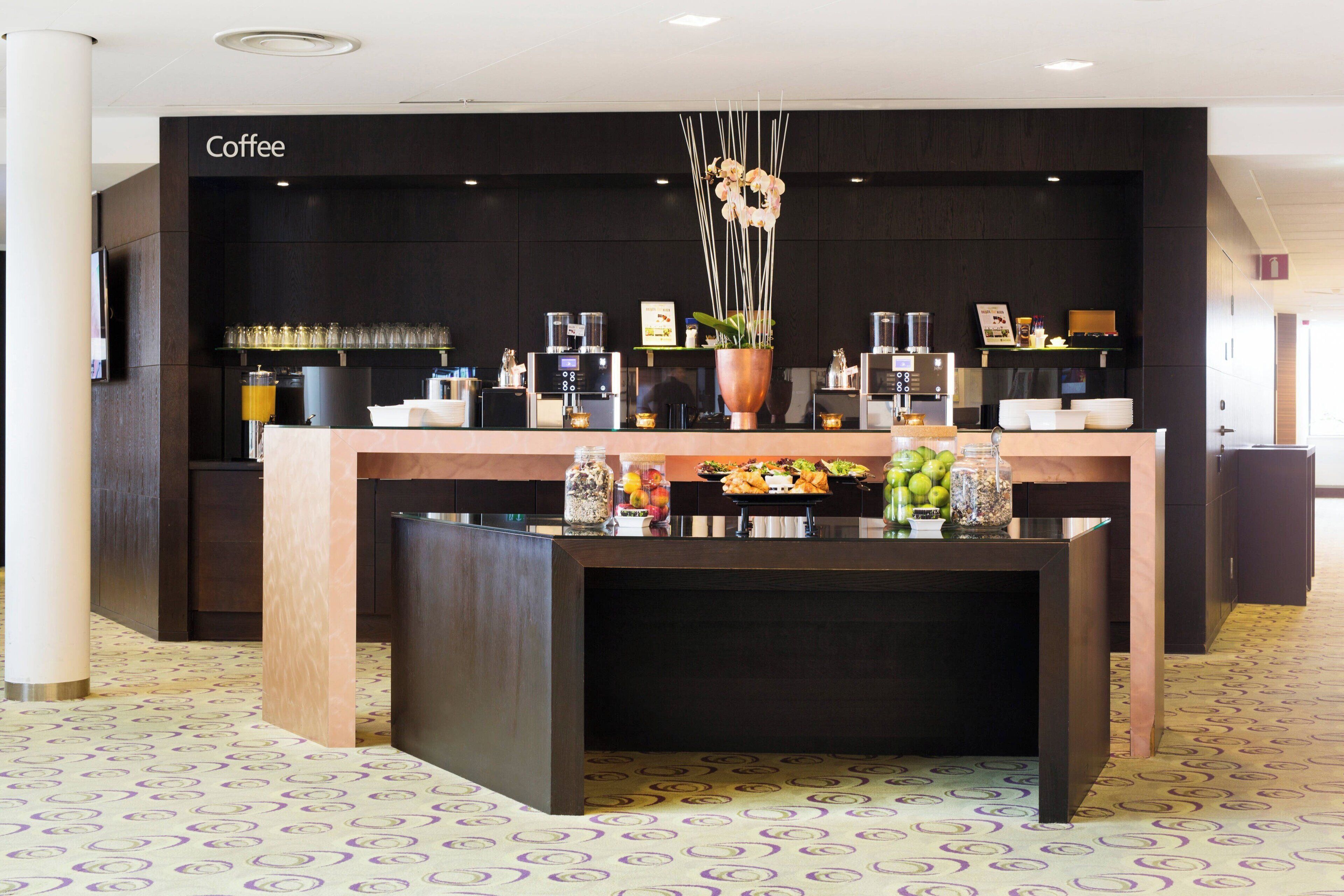 A coffee station with a dark counter, a large vase with flowers, and various coffee-making equipment.