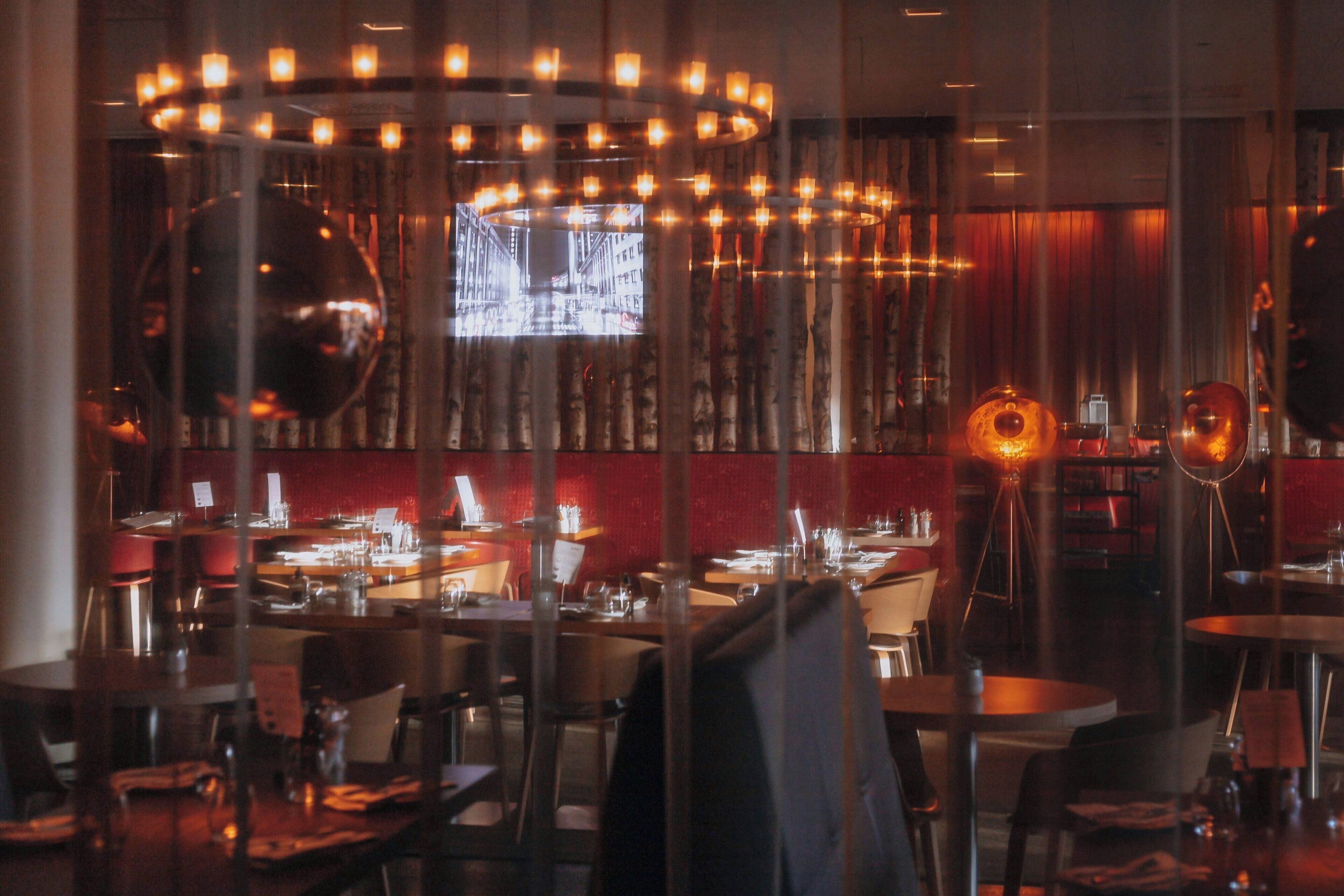 A restaurant interior with round tables, chairs, and a central chandelier.