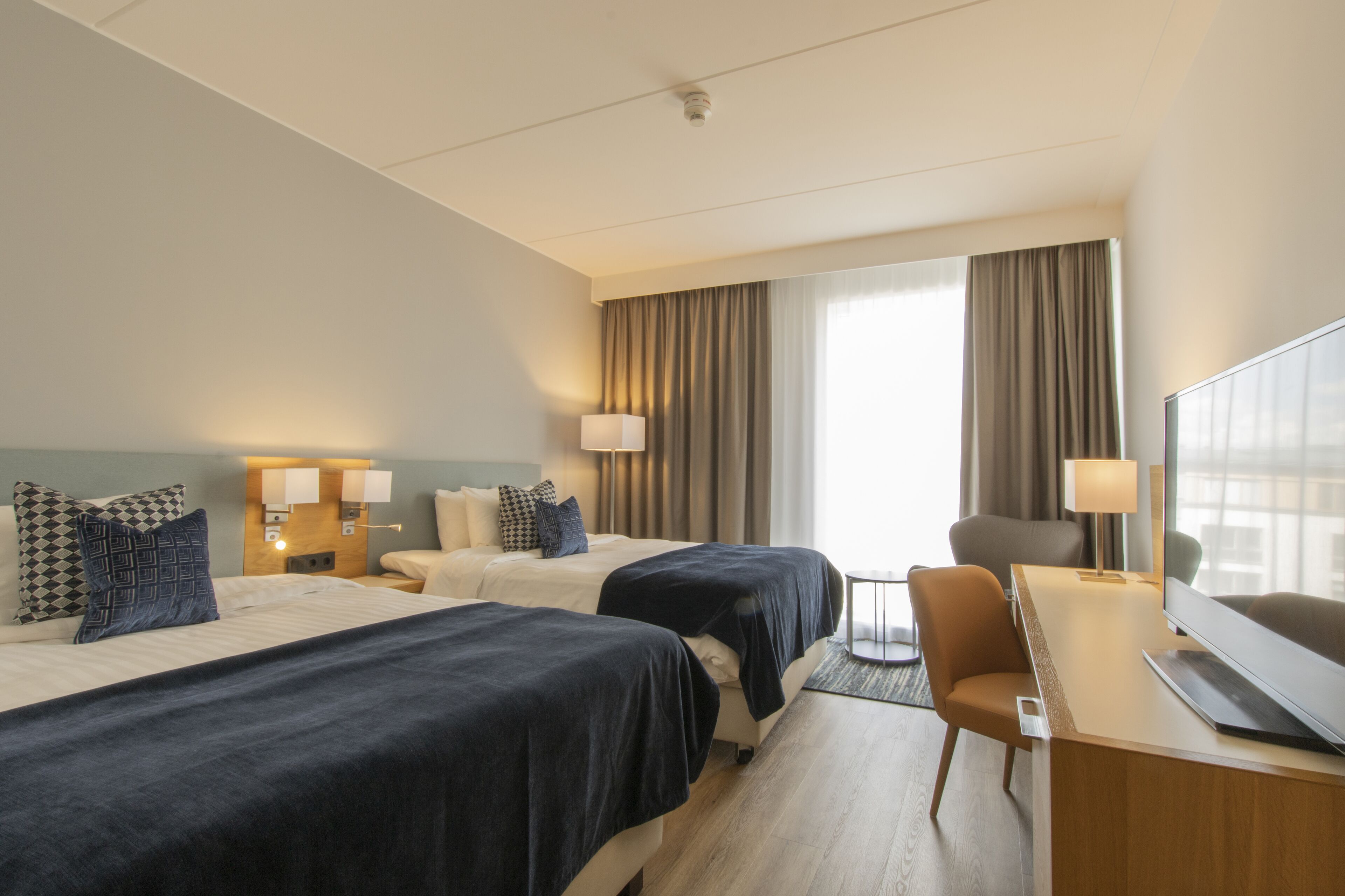 A hotel room with two beds, a desk, a chair, and a TV.