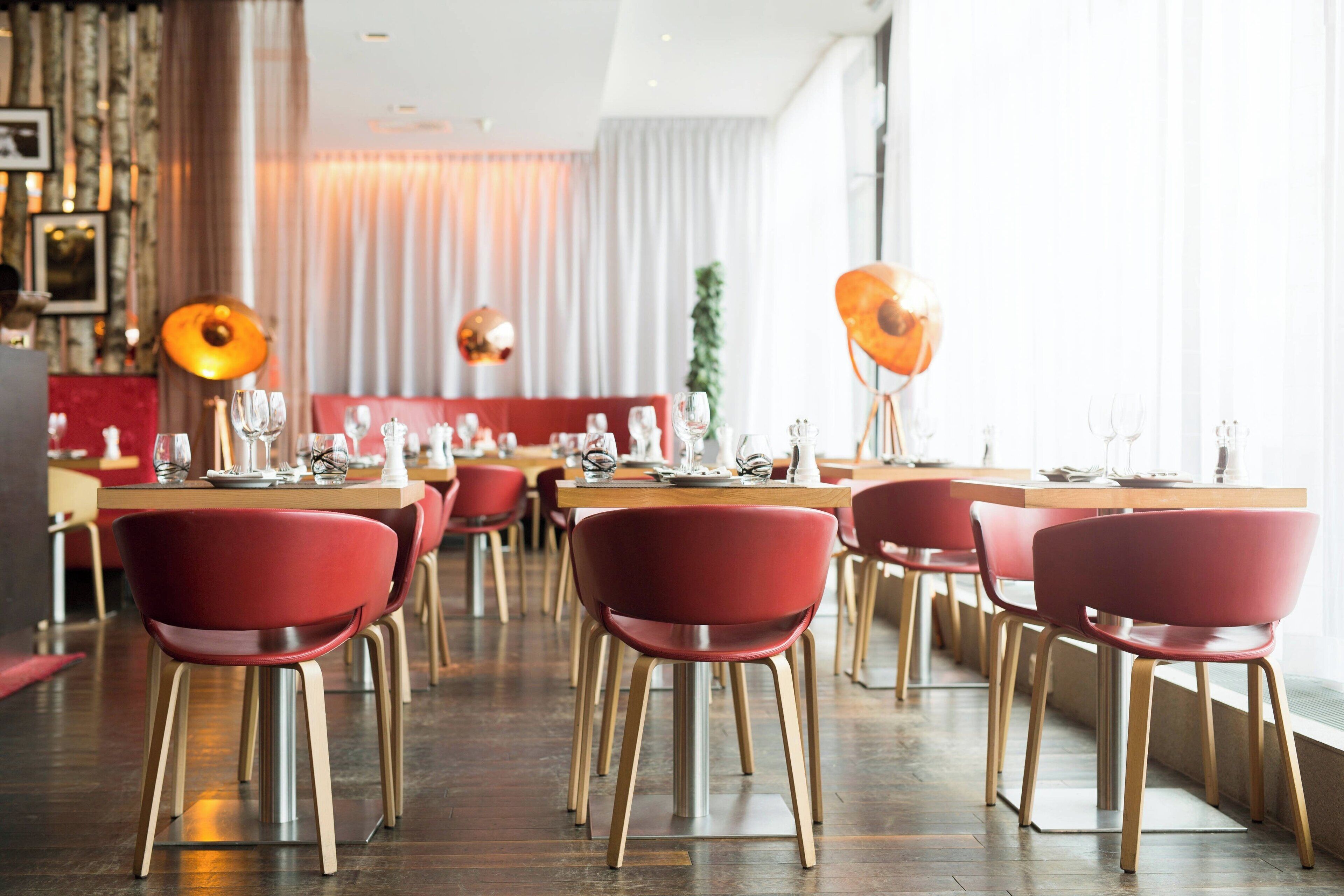 A restaurant with red chairs, wooden tables, and pendant lights.