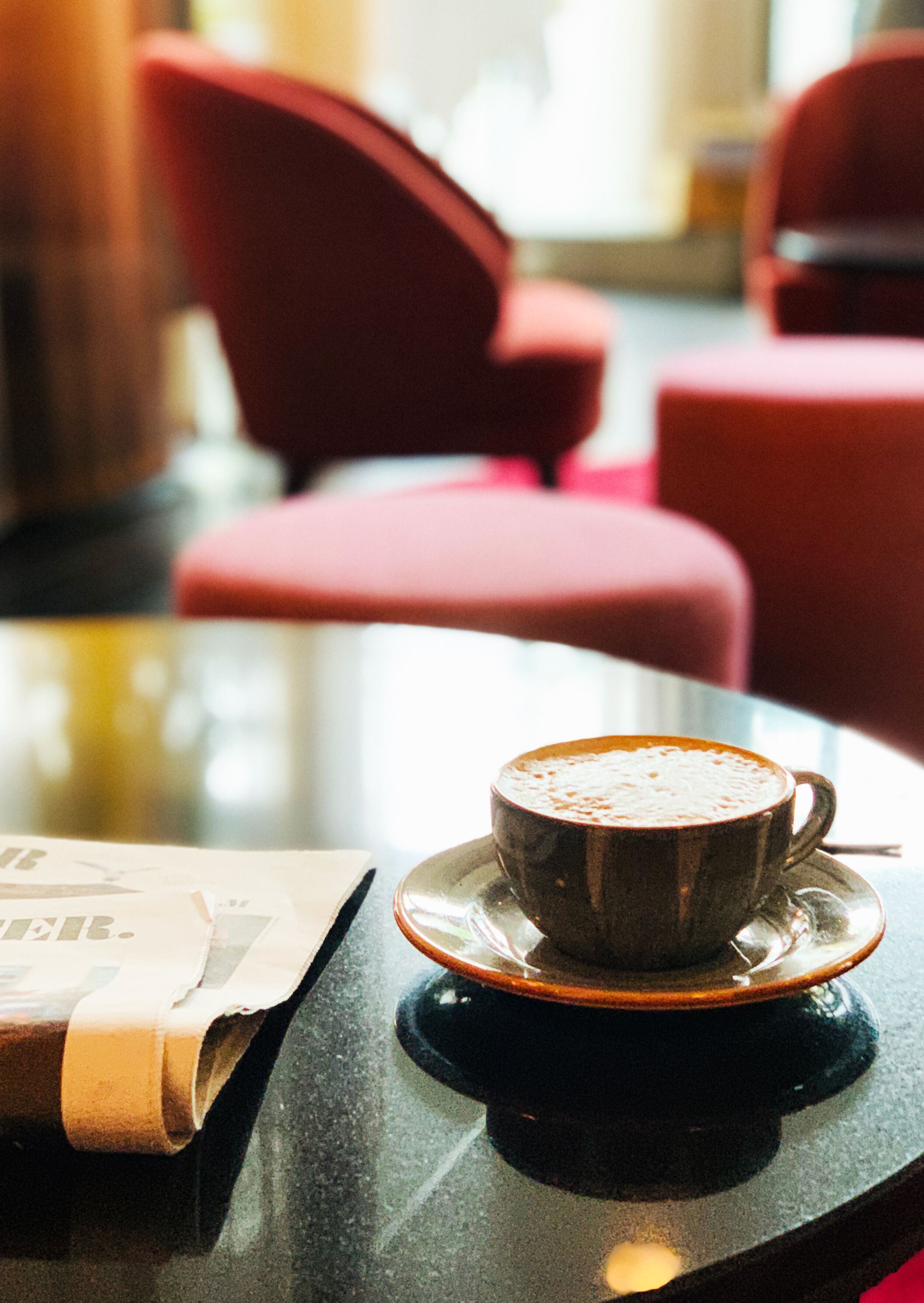 A cup of coffee on a saucer on a table with a newspaper.