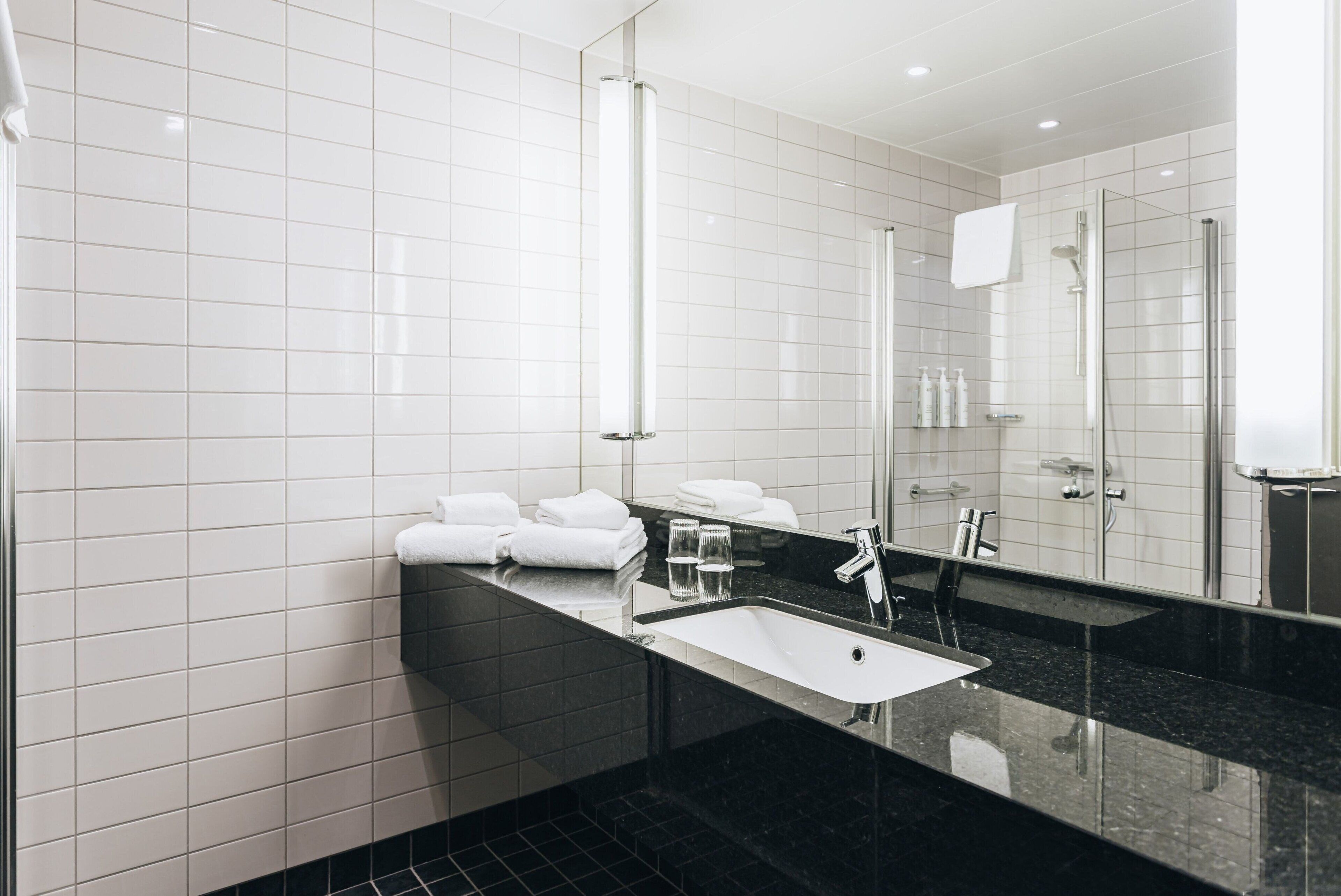 Een moderne badkamer met een grote spiegel, een zwart aanrecht en een witte wastafel.