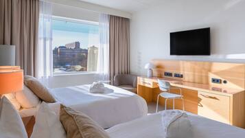 A hotel room with two beds, a desk, a chair, a TV, and a window with a city view.