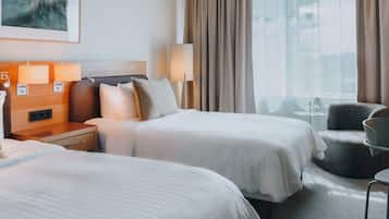 A hotel room with two beds, a sitting area, and a large window with curtains.
