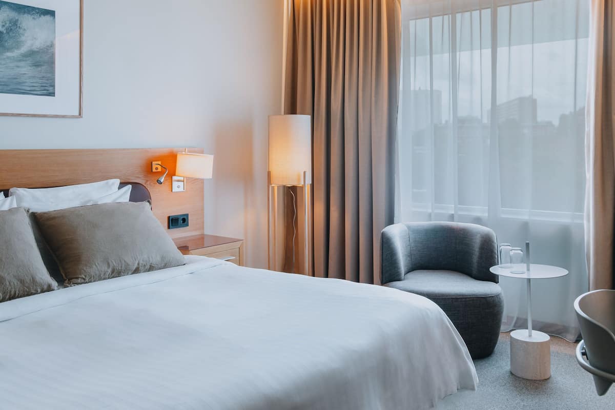 Habitación de hotel con cama, una silla, una mesa y ventana con cortinas.