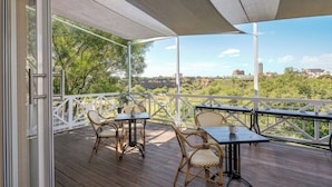 Un espacio al aire libre cubierto con una mesa y sillas, con vistas a zonas verdes y edificios a lo lejos.