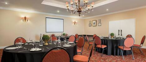 A conference room with multiple tables, chairs, a chandelier, and a projector screen.