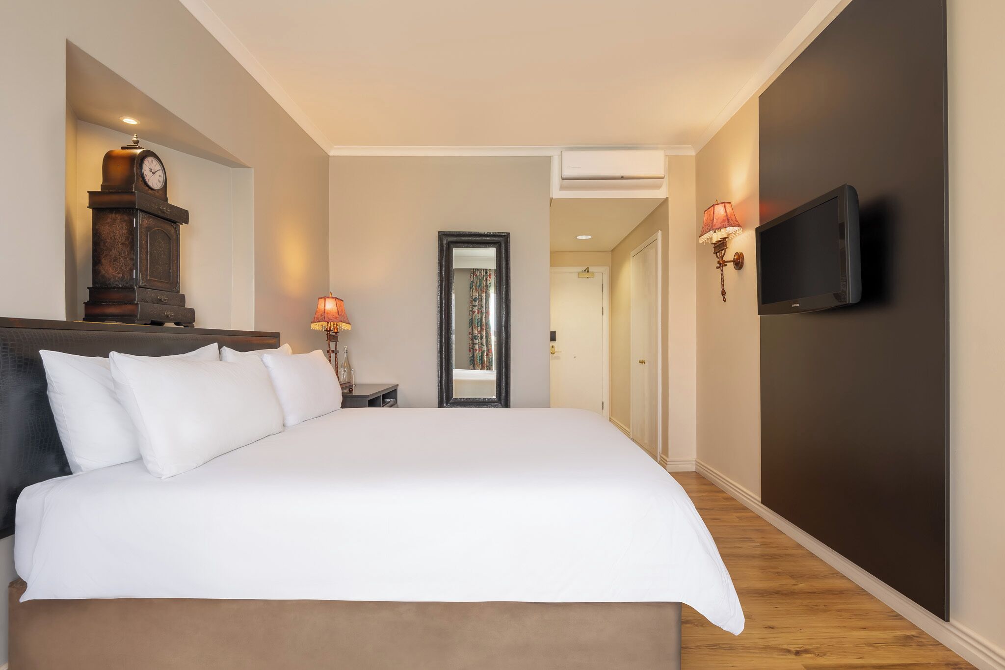 A hotel room with a large bed, a television mounted on the wall, and a nightstand with a lamp.