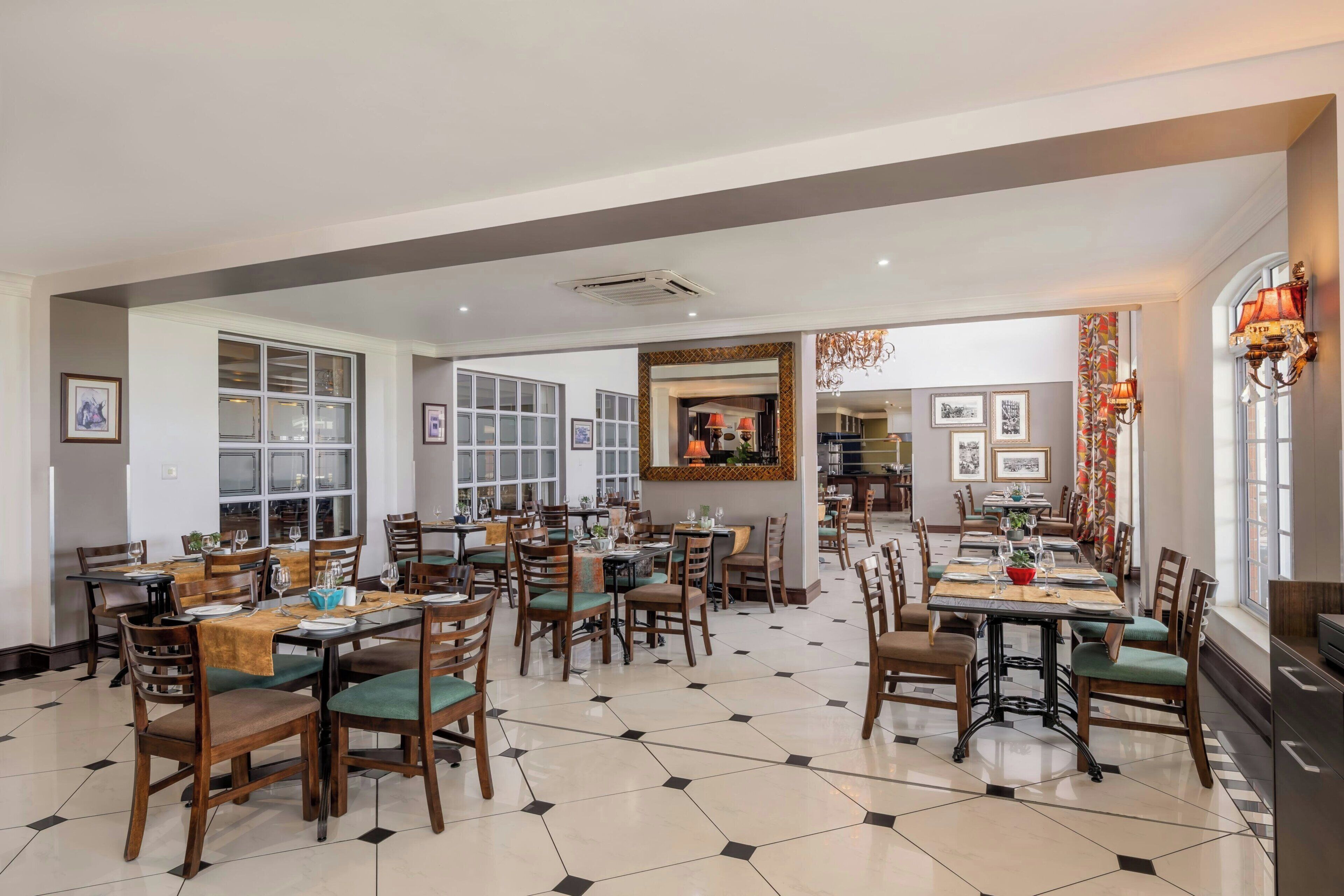 A spacious dining area with multiple tables and chairs, large windows, and a central decorative wall.