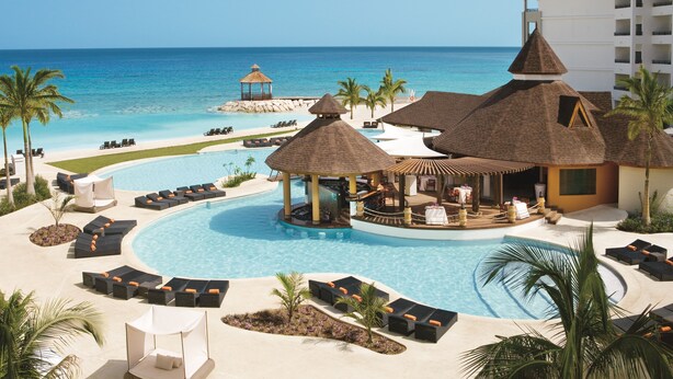 A resort with a large pool, lounge areas, and a view of the ocean.