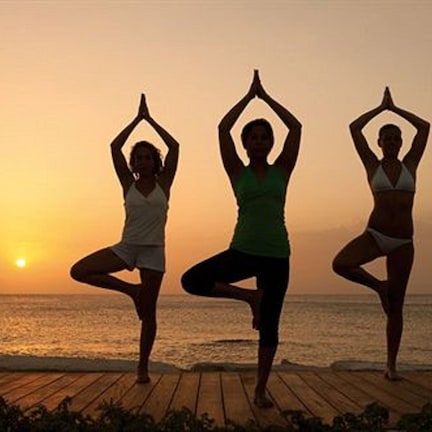 Three people performing yoga on a wooden deck by the ocean at sunset.