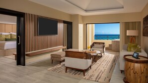 A spacious room with a balcony, a large flat-screen TV, a ceiling fan, and a view of the ocean.
