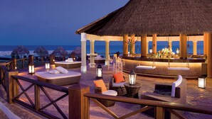 A beachside lounge with thatched-roof seating and a bar area, overlooking the ocean.