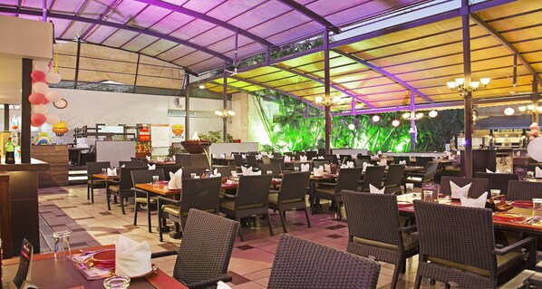A restaurant with outdoor seating, tables with chairs, a counter, and a decorative wall with plants. - Sayaji Indore (Indore)