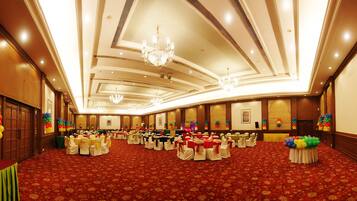 A spacious banquet hall with round tables, chandeliers, and a red carpeted floor.