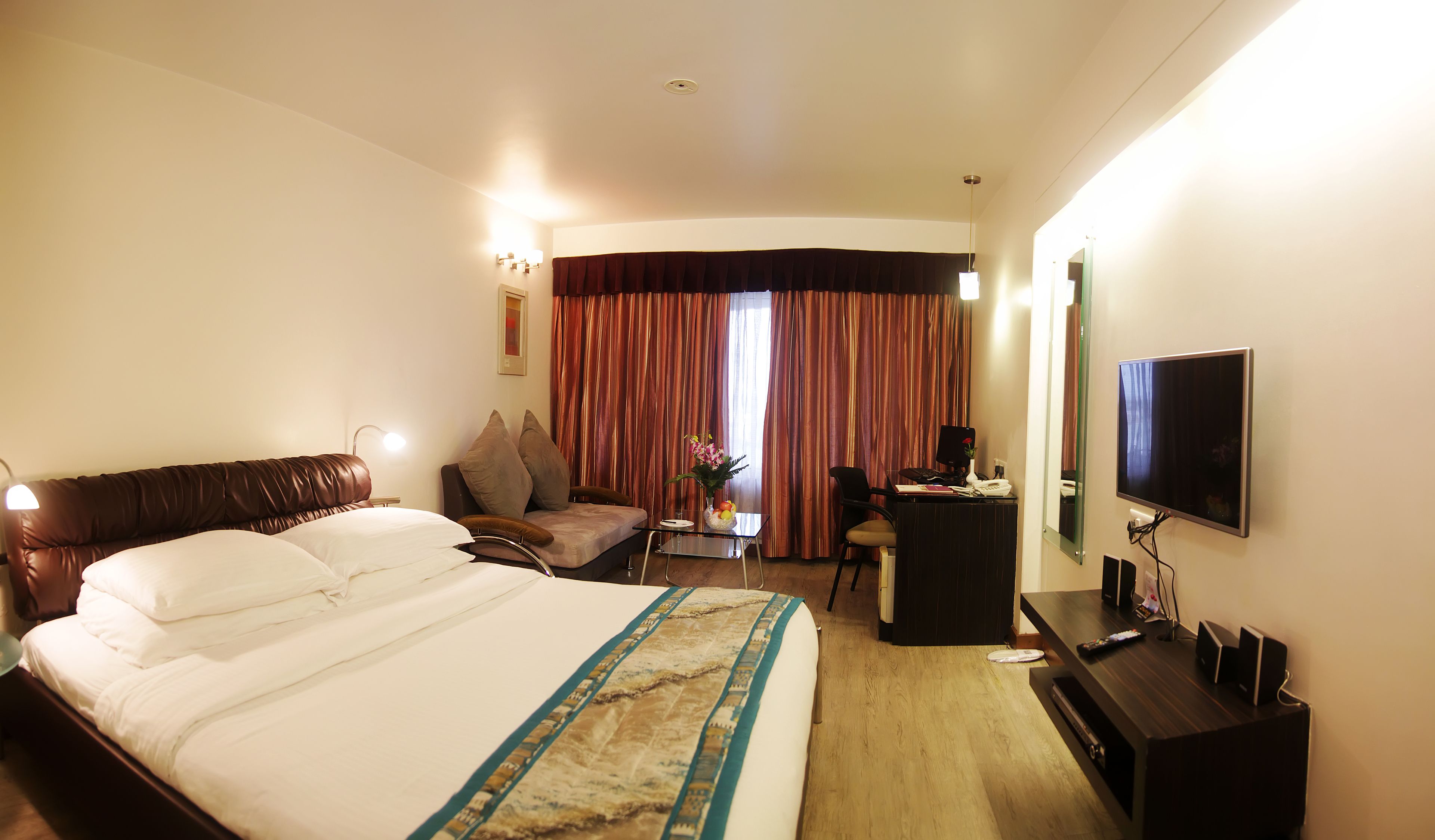 A hotel room with a large bed, a desk with a computer, a TV, and a chair.