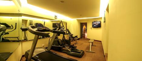A hotel gym with treadmills, elliptical machines, and a TV screen.