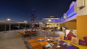 A rooftop dining area with tables and chairs, a decorative sculpture, and a view of the city at night. - Sayaji Indore (Indore)